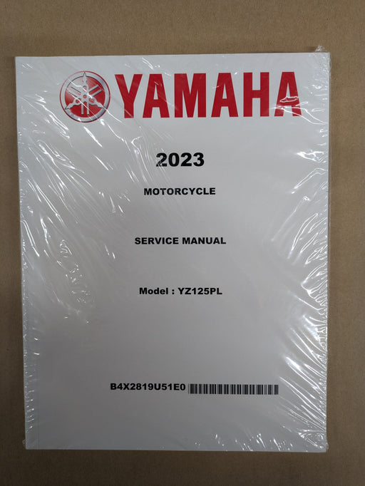 A Yamaha 2023 motorcycle service manual, sealed in clear plastic wrap, placed on a brown cardboard background.
