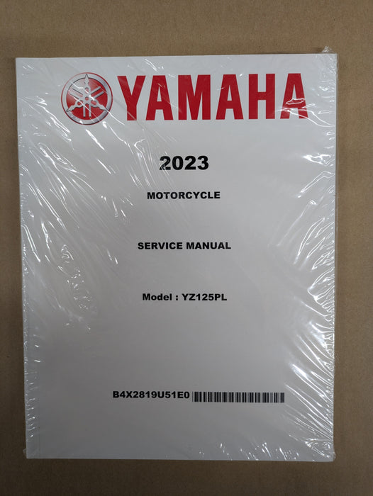 A Yamaha 2023 motorcycle service manual, sealed in clear plastic wrap, placed on a brown cardboard background.